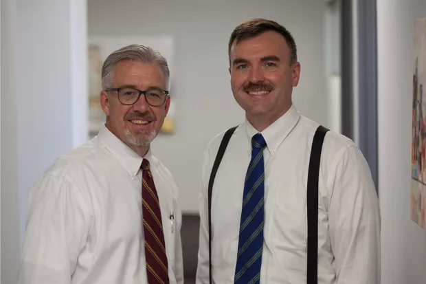 Mark and Tim strike a pose in the hallway of their office. The professional setting is evident from the modern decor and well-lit surroundings.